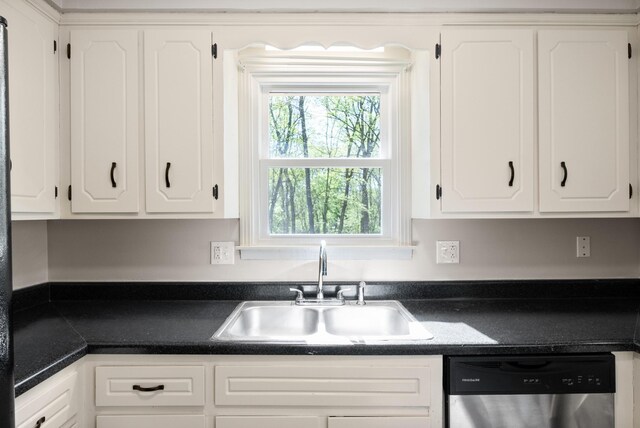 kitchen featuring dark countertops, stainless steel dishwasher, white cabinetry, and a sink