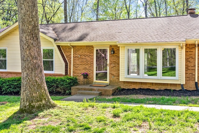 ranch-style home featuring a chimney, brick siding, and a shingled roof