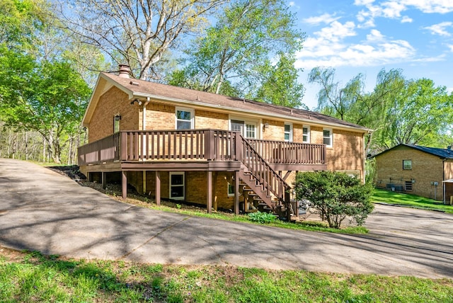 rear view of property with stairway, a chimney, aphalt driveway, brick siding, and a deck