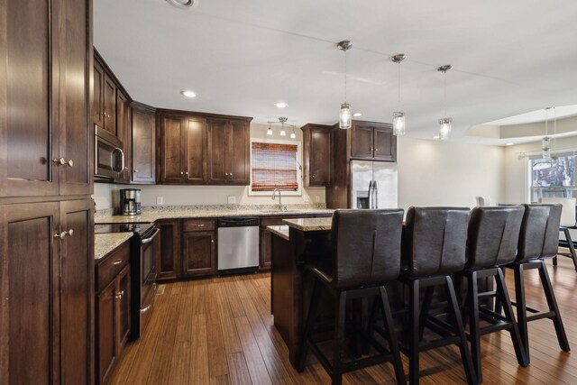 kitchen featuring dark wood-style flooring, a sink, a breakfast bar, dark brown cabinetry, and appliances with stainless steel finishes