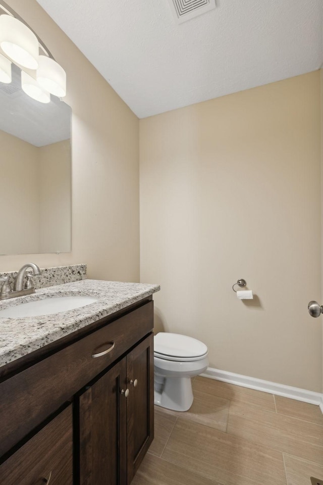 half bath featuring visible vents, baseboards, vanity, and toilet