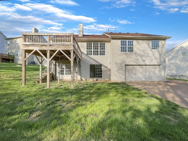rear view of house with driveway, a chimney, a wooden deck, an attached garage, and a lawn
