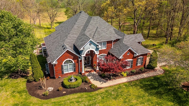 traditional-style home with a forest view, a shingled roof, brick siding, and a front yard