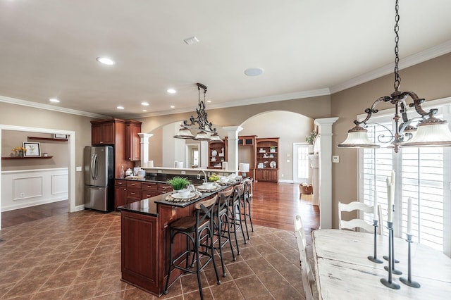kitchen featuring arched walkways, freestanding refrigerator, crown molding, and decorative columns
