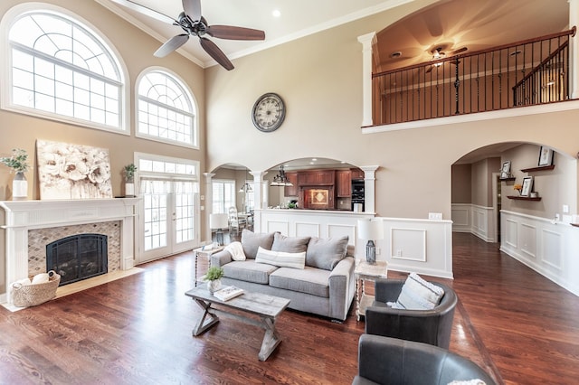 living room featuring arched walkways, decorative columns, a ceiling fan, wood finished floors, and crown molding