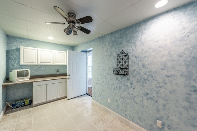 kitchen with wallpapered walls, a ceiling fan, light tile patterned floors, baseboards, and white cabinetry