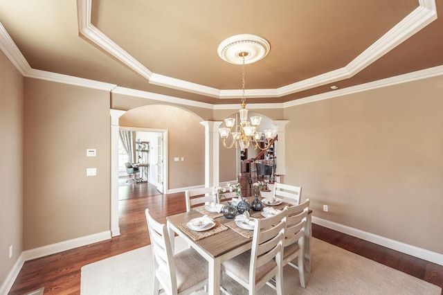 dining room with arched walkways, decorative columns, wood finished floors, crown molding, and a raised ceiling
