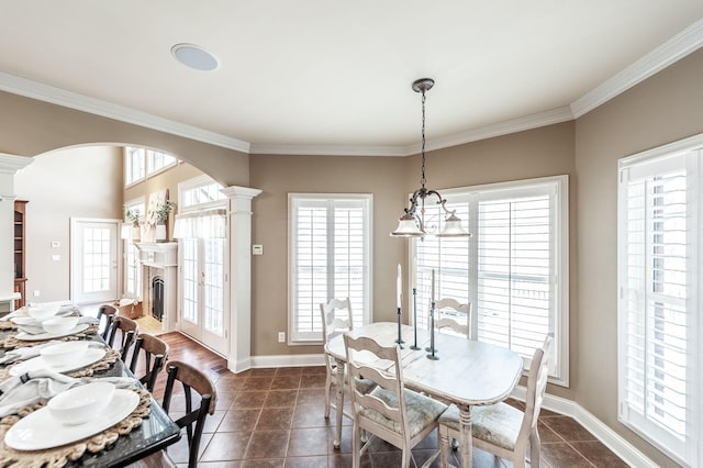 dining area with crown molding, arched walkways, a fireplace, baseboards, and ornate columns