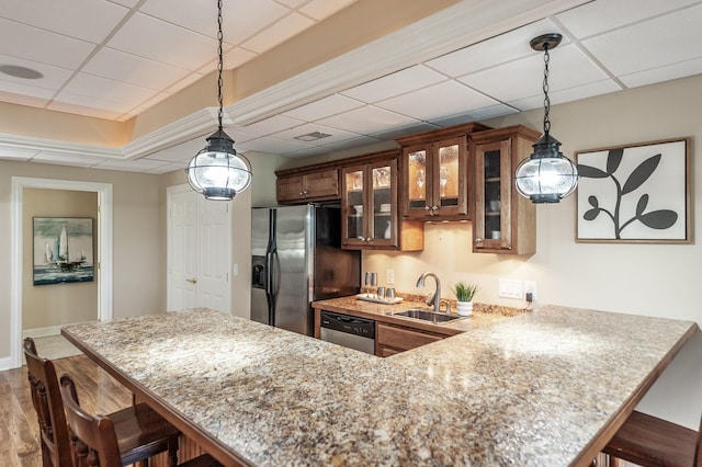 kitchen with a sink, glass insert cabinets, stainless steel appliances, a kitchen bar, and a peninsula
