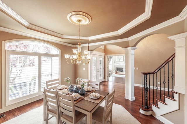 dining room featuring dark wood-style floors, arched walkways, ornate columns, a fireplace, and a raised ceiling
