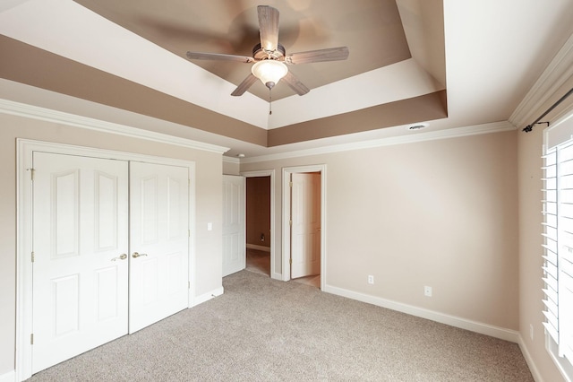 unfurnished bedroom with light colored carpet, baseboards, crown molding, and a raised ceiling