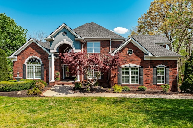 view of front of property with brick siding, roof with shingles, and a front yard