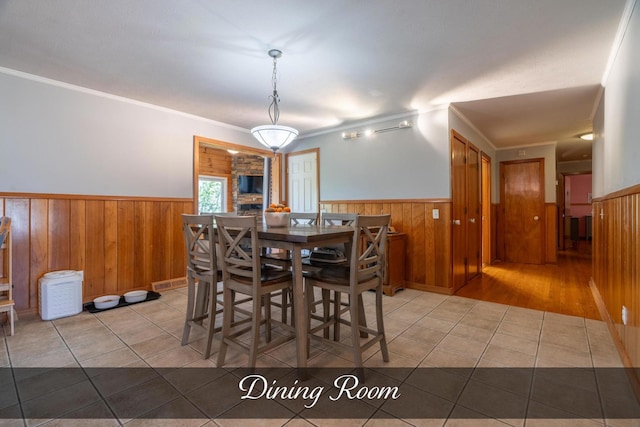 tiled dining space with ornamental molding, a wainscoted wall, and wood walls