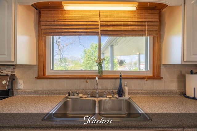kitchen featuring white cabinets, dark countertops, decorative backsplash, and a sink