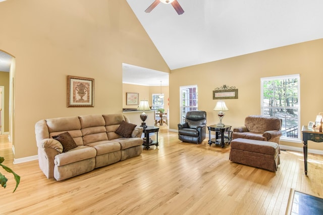 living area featuring a ceiling fan, arched walkways, baseboards, light wood-style flooring, and high vaulted ceiling