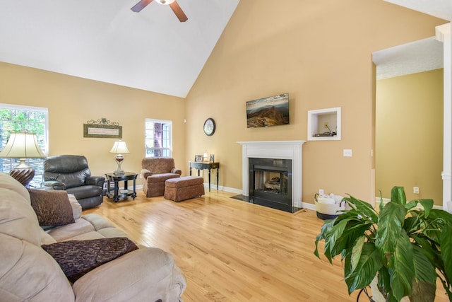living area featuring a fireplace with flush hearth, plenty of natural light, a ceiling fan, wood finished floors, and high vaulted ceiling