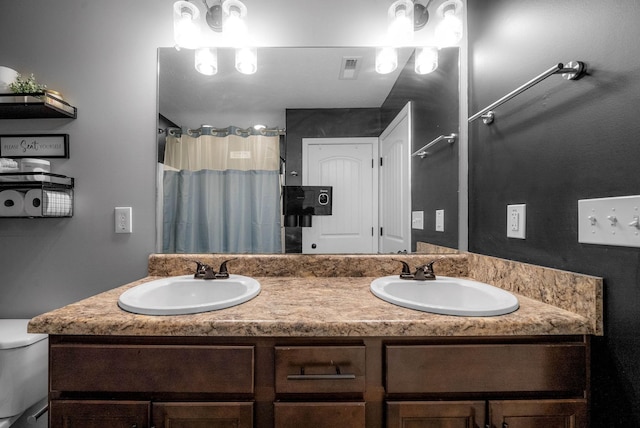 bathroom featuring double vanity, visible vents, toilet, and a sink