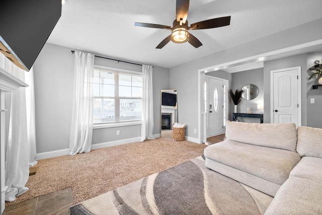 carpeted living area featuring baseboards, a glass covered fireplace, and ceiling fan