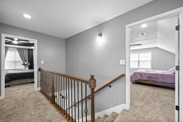 corridor featuring lofted ceiling, carpet flooring, a textured ceiling, and visible vents