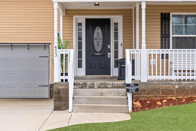 view of exterior entry with a garage, a porch, and concrete driveway