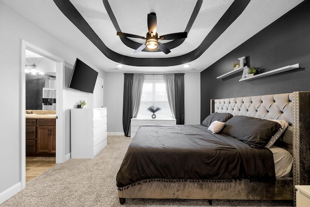 bedroom featuring light colored carpet, baseboards, ensuite bath, and a raised ceiling