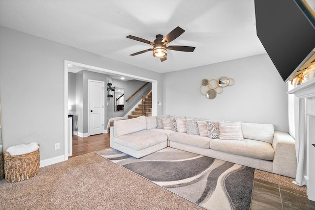 carpeted living room with stairway, ceiling fan, baseboards, and wood finished floors