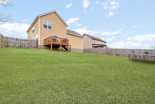 rear view of house with a fenced backyard, a trampoline, a lawn, stairway, and a deck