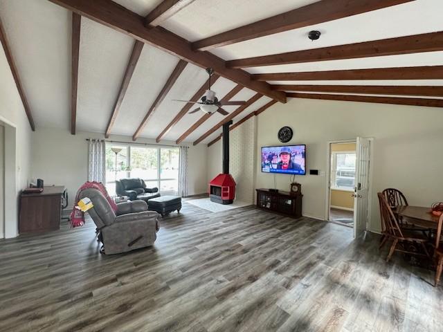 living area featuring plenty of natural light, a wood stove, vaulted ceiling with beams, and wood finished floors