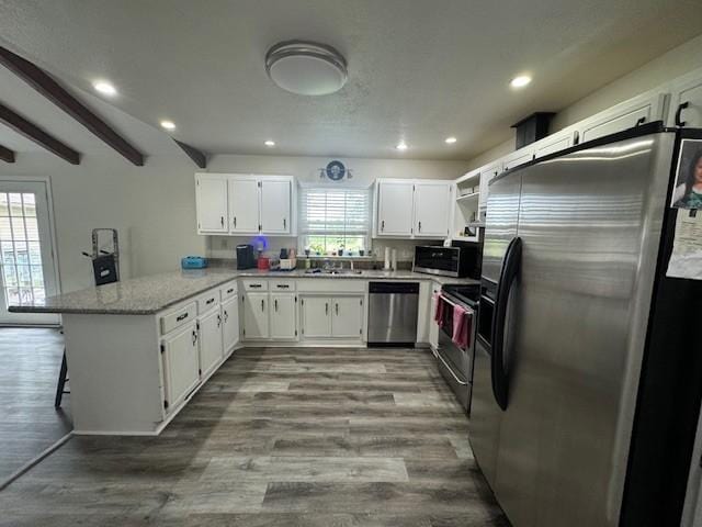 kitchen featuring white cabinets, stainless steel appliances, a peninsula, dark wood-style flooring, and recessed lighting