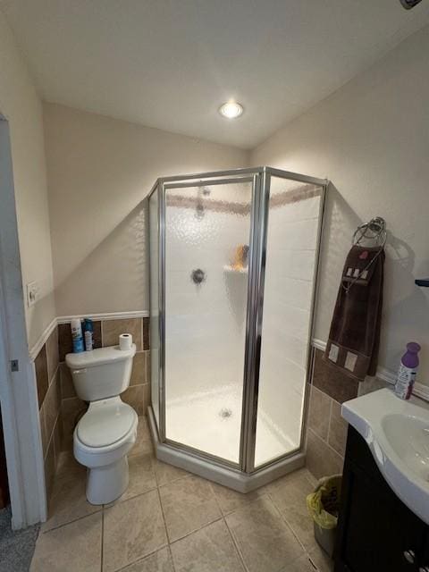 bathroom with a shower stall, tile patterned flooring, toilet, vanity, and tile walls