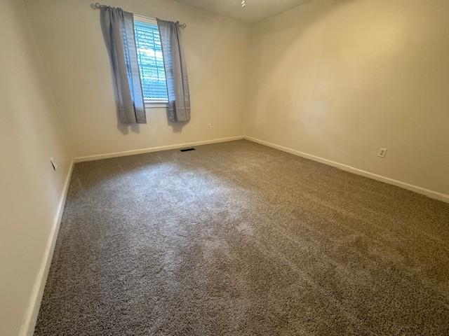 unfurnished room with dark carpet, visible vents, and baseboards
