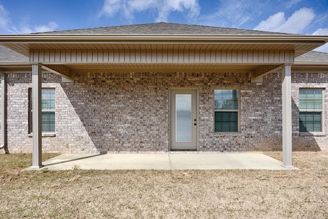 entrance to property with brick siding, a patio area, and a shingled roof