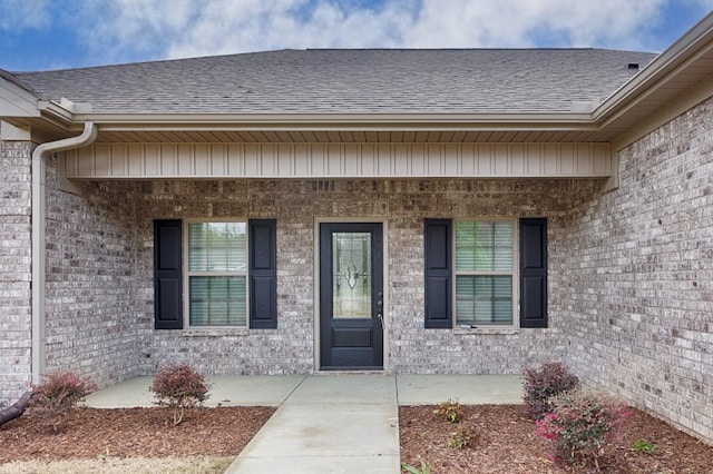 doorway to property featuring brick siding, roof with shingles, and a patio