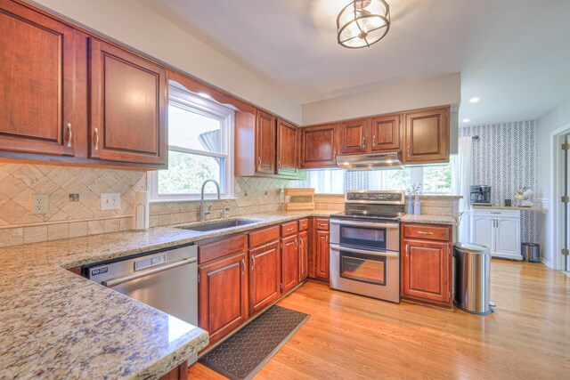kitchen featuring light wood-style flooring, a sink, decorative backsplash, under cabinet range hood, and appliances with stainless steel finishes