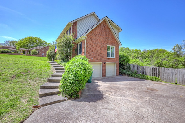 view of side of home with driveway, fence, brick siding, an attached garage, and a yard