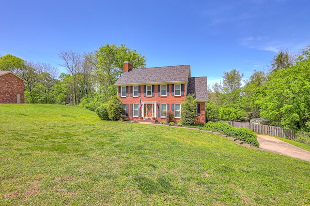 colonial-style house featuring brick siding, a front lawn, fence, and a chimney