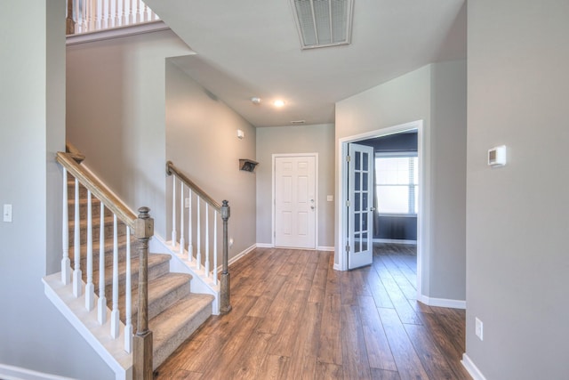 foyer entrance with baseboards, visible vents, hardwood / wood-style flooring, and stairway
