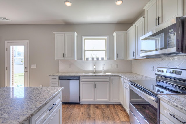 kitchen with wood finished floors, a sink, stainless steel appliances, white cabinetry, and visible vents