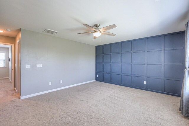 unfurnished room with a decorative wall, a ceiling fan, light colored carpet, baseboards, and visible vents