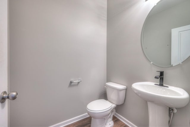 bathroom featuring wood finished floors, toilet, baseboards, and a sink