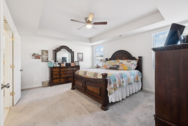 bedroom with a tray ceiling, baseboards, and light carpet