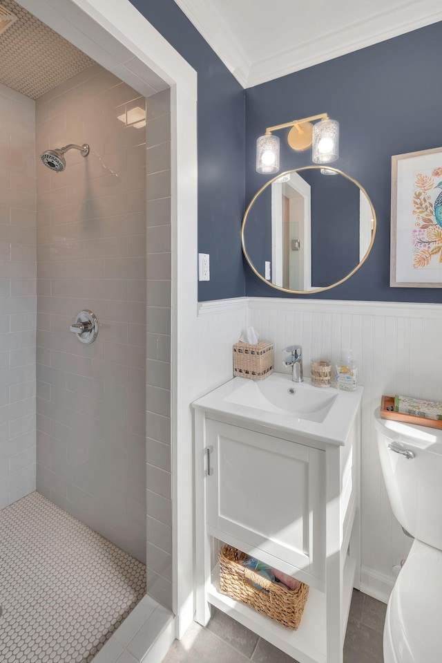 full bath featuring a tile shower, toilet, vanity, and a wainscoted wall