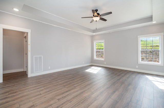 spare room featuring ceiling fan, a tray ceiling, wood finished floors, and visible vents