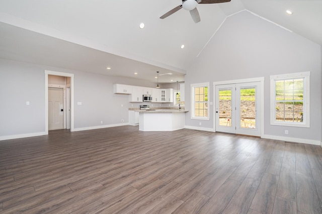 unfurnished living room with high vaulted ceiling, ceiling fan, baseboards, and dark wood-style flooring