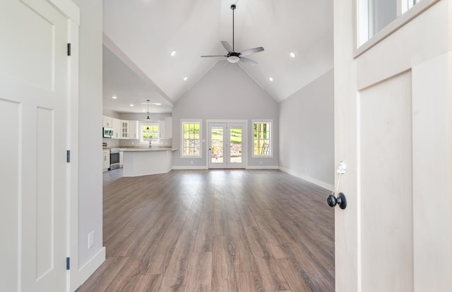unfurnished living room with wood finished floors, baseboards, ceiling fan, high vaulted ceiling, and recessed lighting