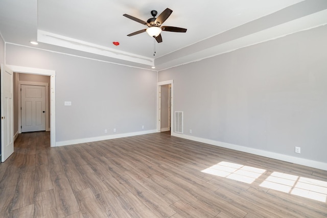empty room featuring visible vents, wood finished floors, baseboards, ceiling fan, and a raised ceiling