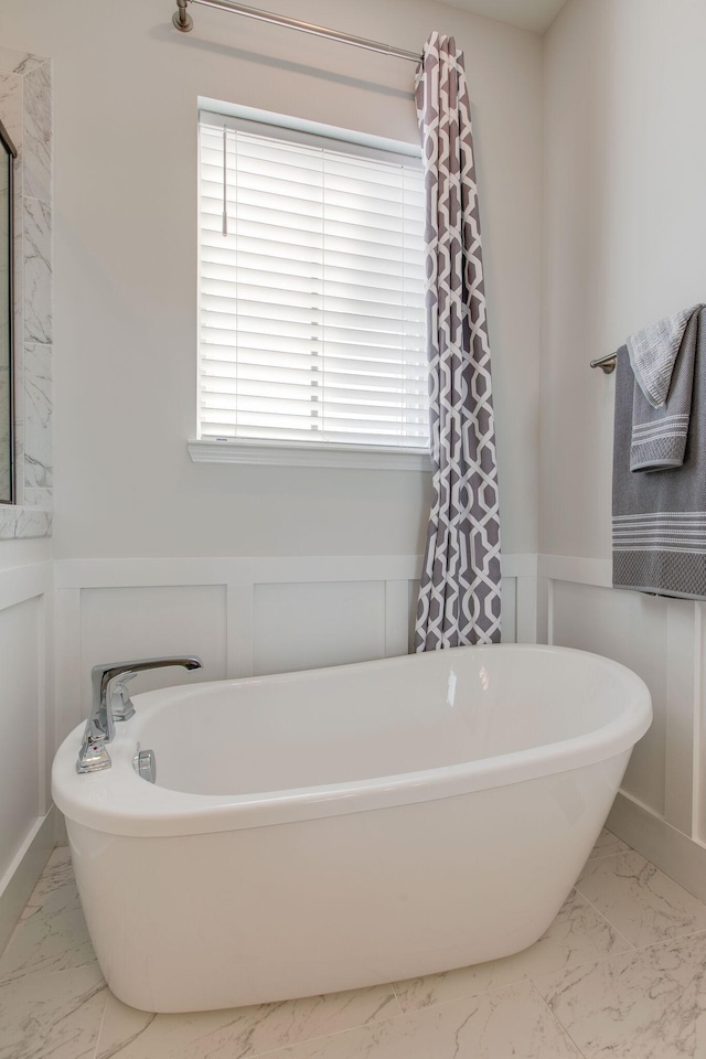 full bath with a wainscoted wall, marble finish floor, a freestanding bath, and a decorative wall