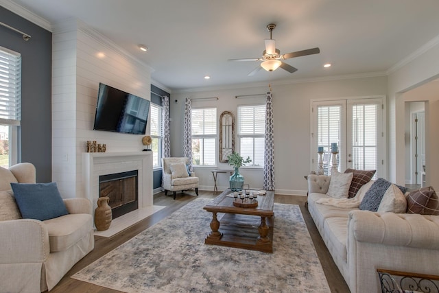living area featuring a fireplace with flush hearth, wood finished floors, crown molding, and ceiling fan