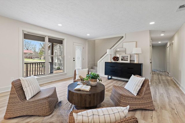 living area featuring light wood finished floors, visible vents, a textured ceiling, and stairway