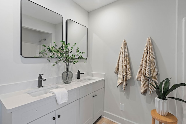 bathroom with wood finished floors, baseboards, a sink, and double vanity